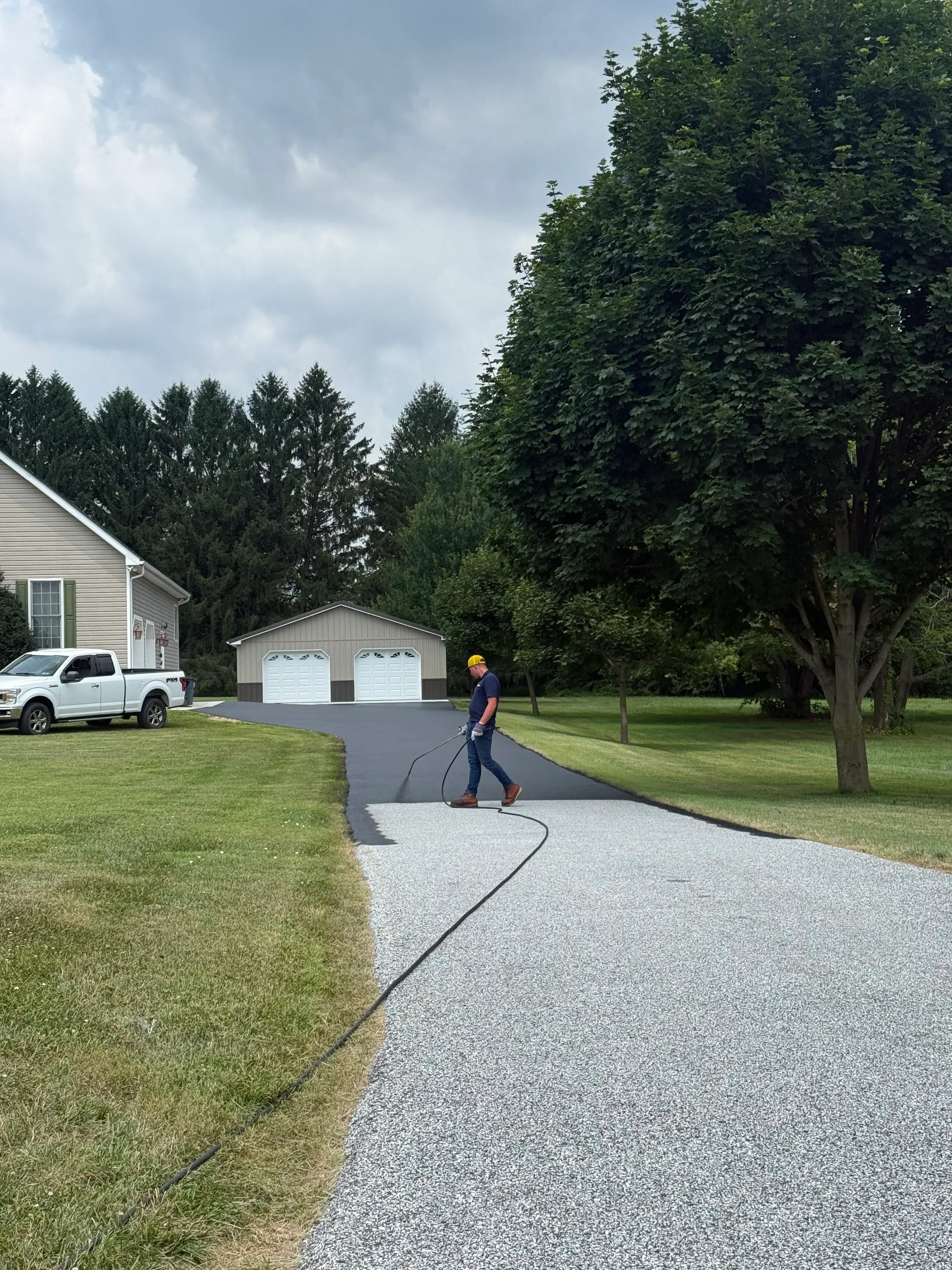 Newly installed dark asphalt driveway with clean edges adjacent to manicured lawn and mature landscaping