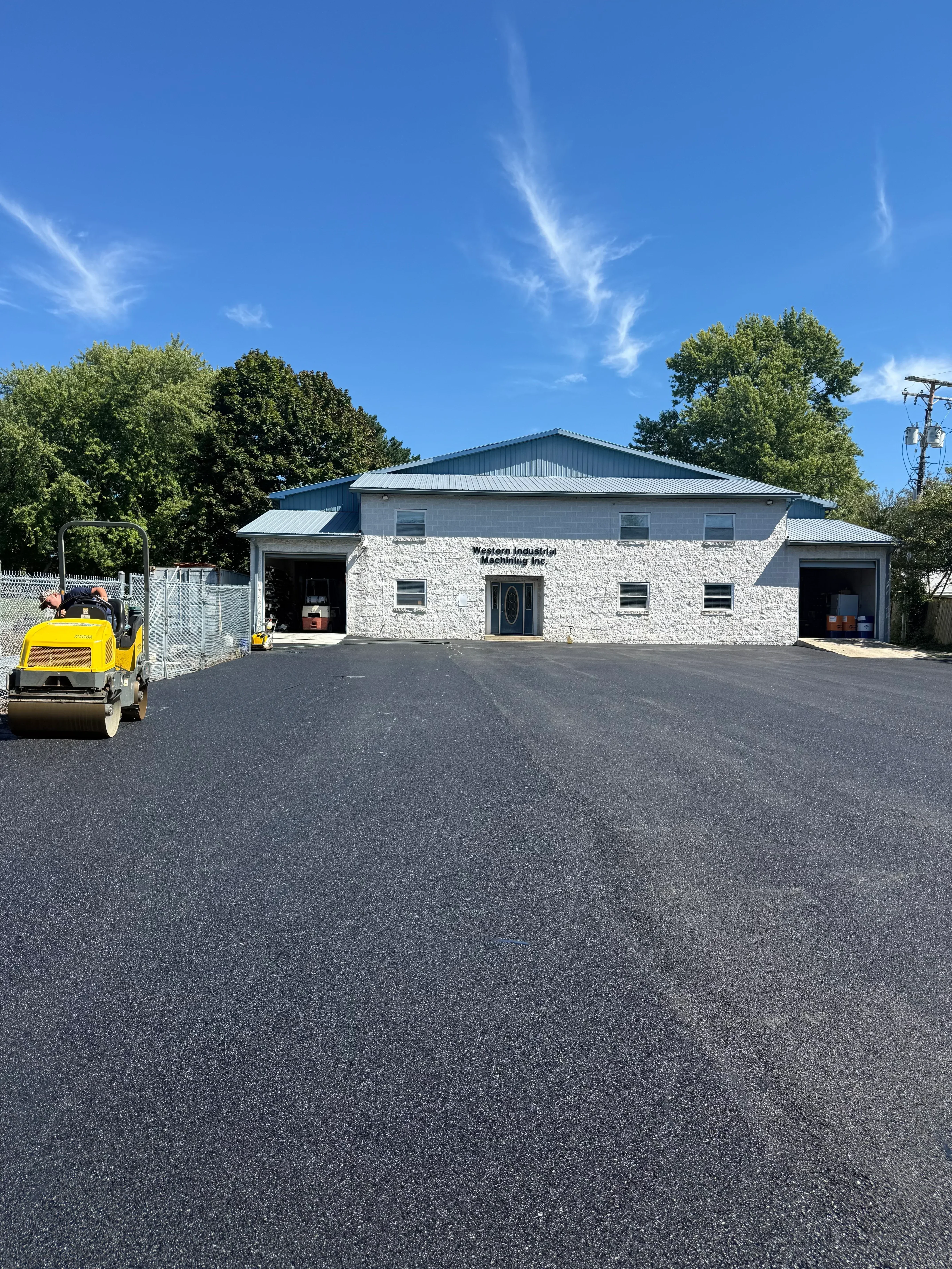 Newly installed black asphalt driveway with compacted surface in front of white brick residential home