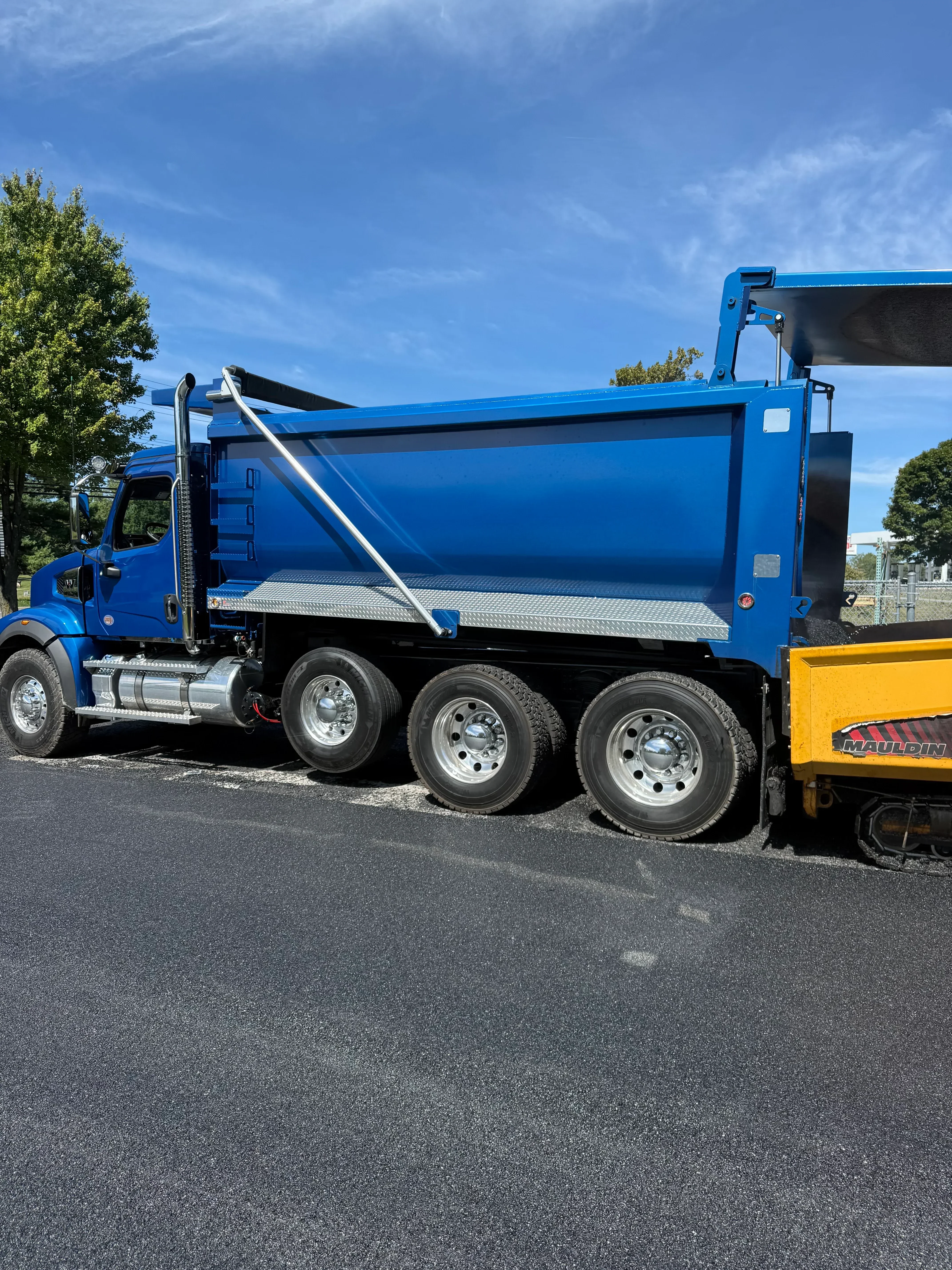 Blue tri-axle dump truck with hydraulic lift gate and aluminum tank for asphalt hauling