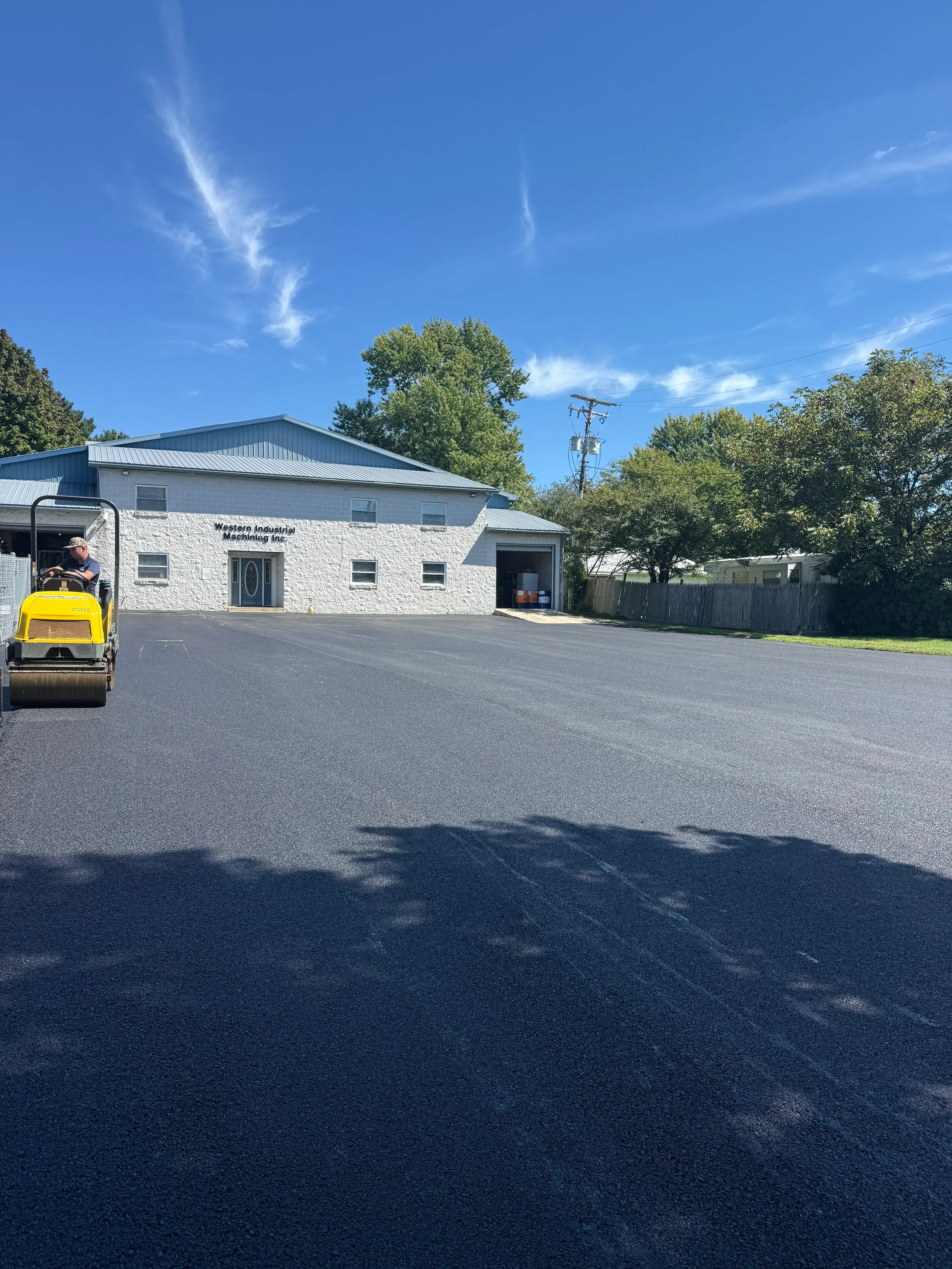 Newly installed black asphalt driveway with compacted surface in front of white stone veneer home