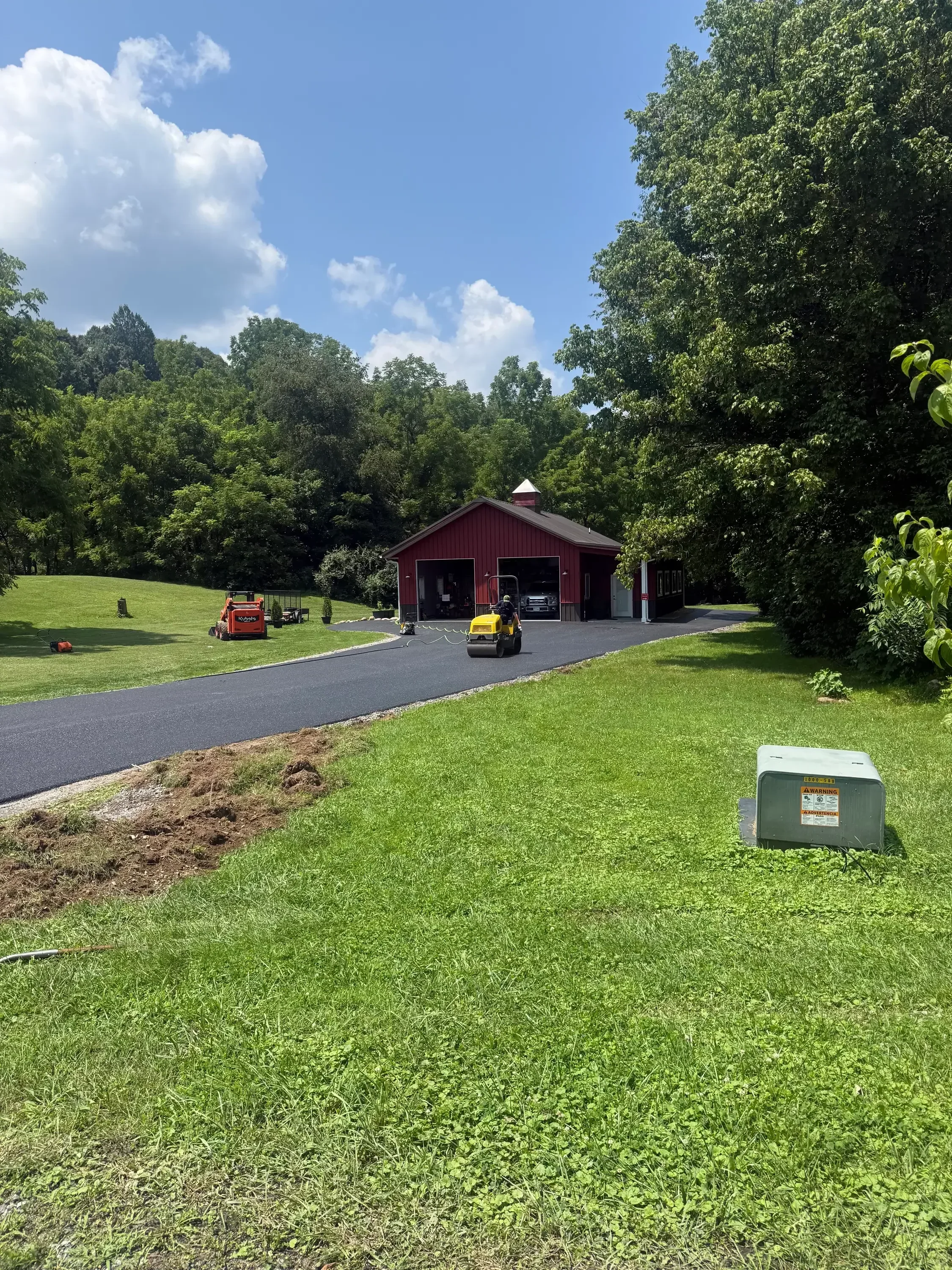 New asphalt driveway with dark finish installed at residential home with mature trees and green lawn