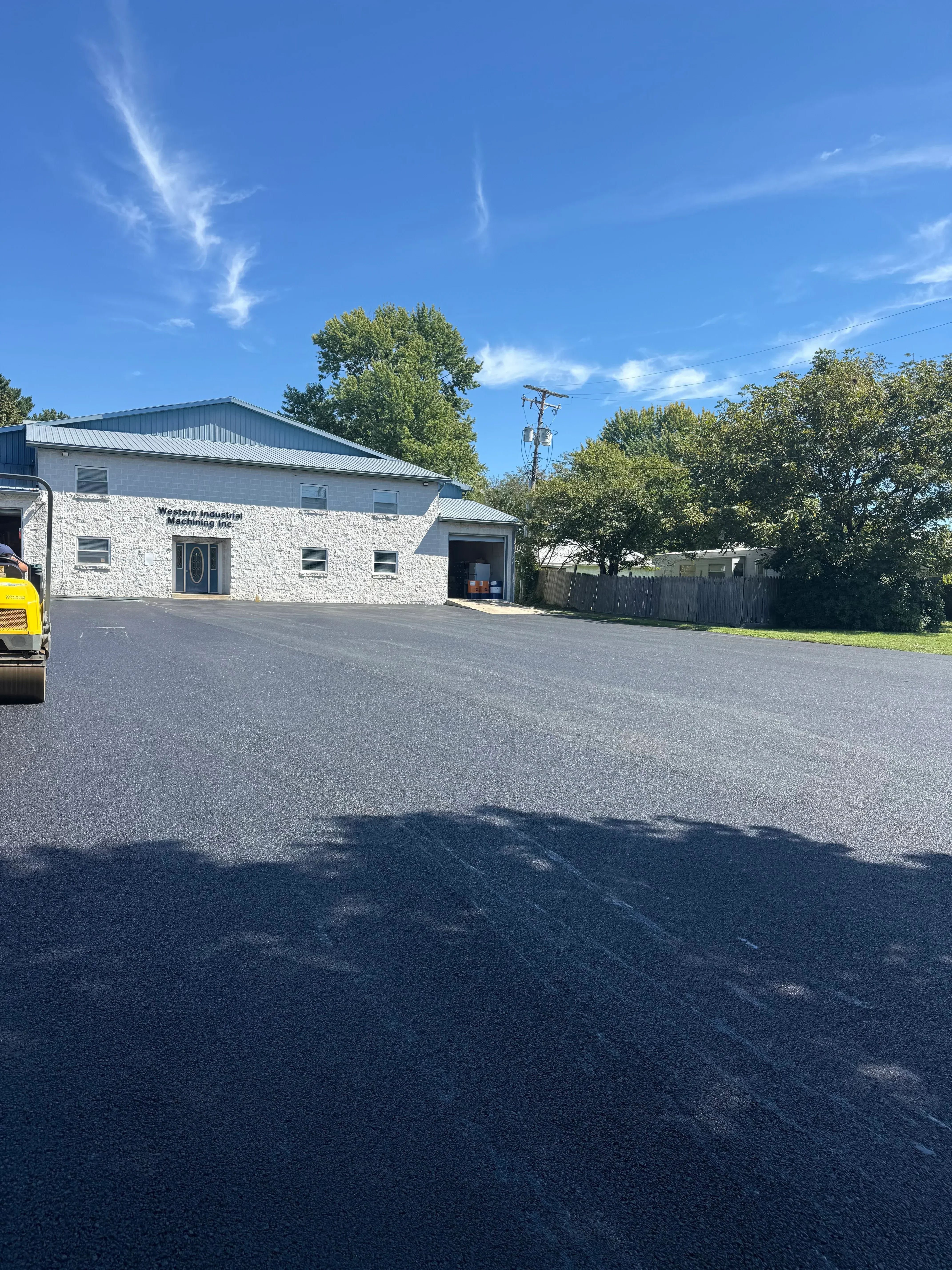 New black asphalt driveway installed at residential home with white brick facade